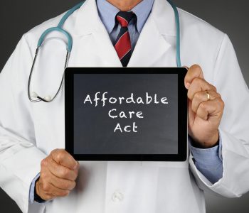 Closeup of a doctor holding a tablet computer with a chalkboard screen with the words Affordable Care Act (Obamacare). Man is unrecognizable.
