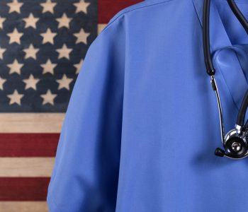 Closeup of medical scrubs with stethoscope against faded boards painted in USA flag background. Healthcare concept for America.
